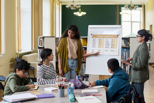 Young female student leading a language class discussion with peers in a classroom - Powered by Adobe