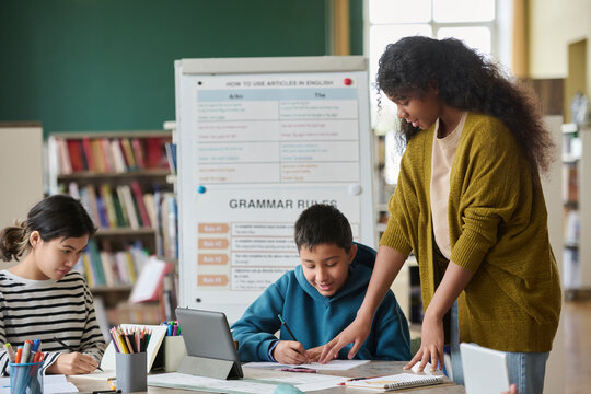 Girl assisting classmates in a language class with grammar rules in the background