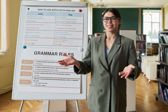 Female teacher conducting language class by board with grammar rules