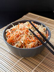 Close-up of a woman's hands mixing shredded white cabbage with carrots
