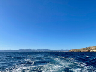 Naklejka premium A distant mountainous horizon across turquoise waters, with a rocky headland under a clear blue sky