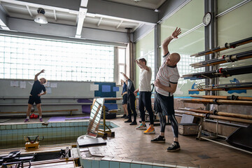 Focused attentive rowers train with coach, do side bends warming up before rowing session in gym....