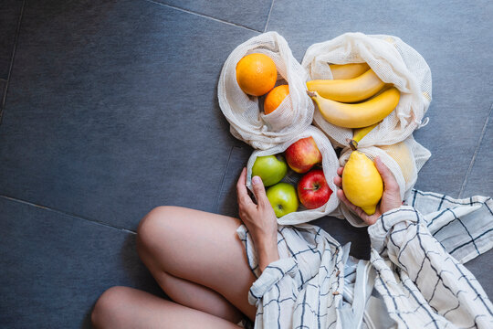 Woman holding fresh fruit in mesh bags promoting zero waste and sustainable lifestyle