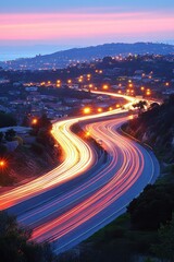 Winding highway illuminated by car lights at twilight with coastal city skyline in background aerial shot