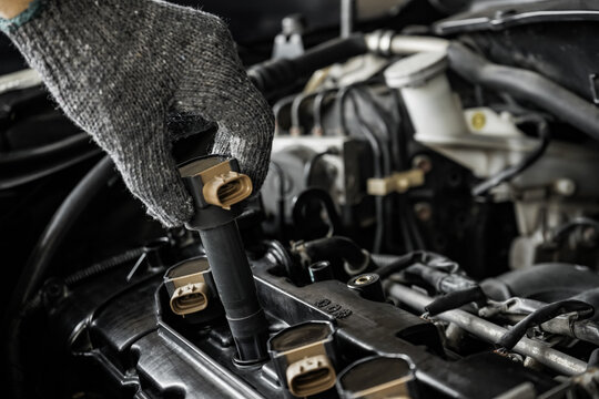 Close-up of a mechanic installing an ignition coil inside the engine compartment.