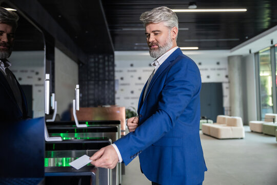 Gray-haired mature business man in dark-blue suit entering office with an access card