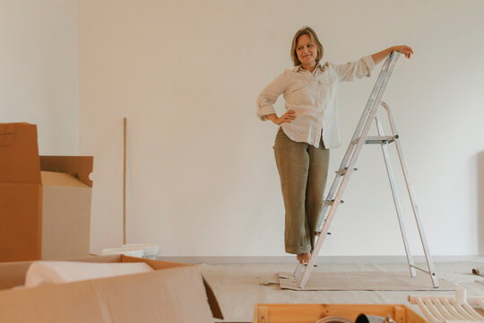 Woman standing on a ladder in an empty room during home renovation