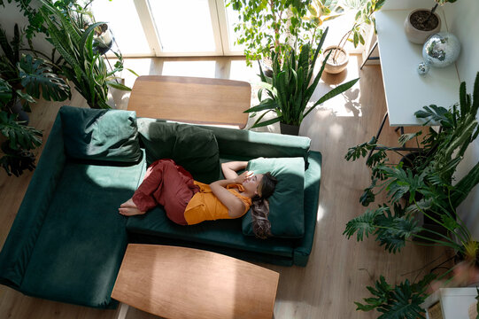 Young woman resting on a green couch in a cozy living room with plants