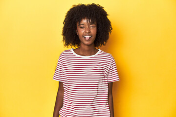 Teen girl in red striped T-shirt, yellow studio backdrop funny and friendly sticking out tongue.