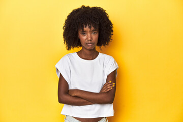 Teen girl in white tank top, yellow studio background unhappy looking in camera with sarcastic...