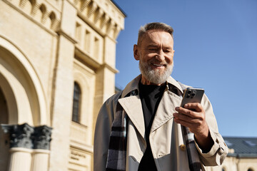 A fashionable senior man strolls through a vibrant city, checking smartphone with a beaming smile.