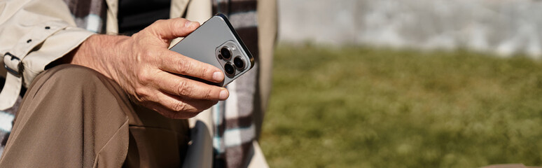 A fashionable senior man dressed in trendy attire, engaging with his smartphone on a beautiful day.