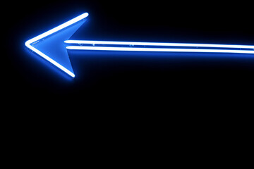 A luminous blue neon arrow points left against a stark black backdrop.  The bright light creates a strong directional cue, highlighting a path or indicating a turn.