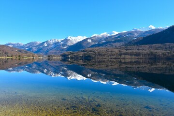 Fototapeta premium View of snow covered mountain peaks in Julian alps and lake Bohinj bellow with a reflection of the mountains on the water in Gorenjska, Slovenia