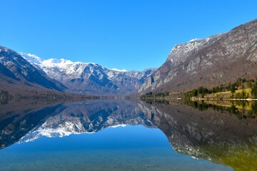 Fototapeta premium View of lake Bohinj and mountain above covered in snow and a reflection of the mountains in the water in Gorenjska, Slovenia