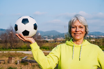 Naklejka premium Senior woman holding soccer ball in nature smiling and promoting healthy lifestyle