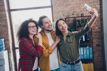 Group of young coworkers taking a selfie in a casual office environment showcasing teamwork, diversity