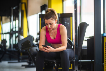 Fototapeta premium Woman checking her phone while taking break at gym