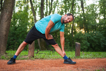 Young sportsman stretching legs before running in nature