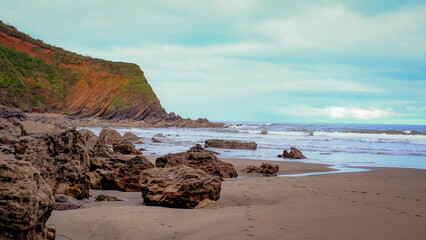 Scenic coastal landscape featuring a rocky beach with large boulders scattered along the shoreline