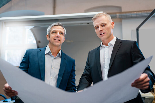 Two confident businessmen holding a plan in a factory