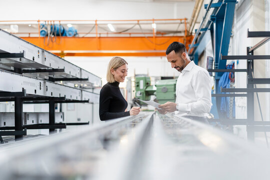 Businessman and woman with papers at metal rods in factory hall