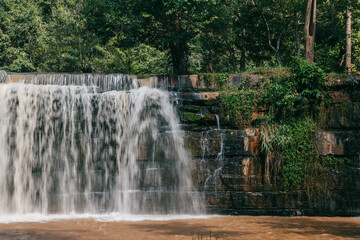 Cascading Waterscape: The raw power and serene beauty of a natural waterfall, cascading gracefully over a tiered stone structure, framed by verdant greenery and lush trees.
