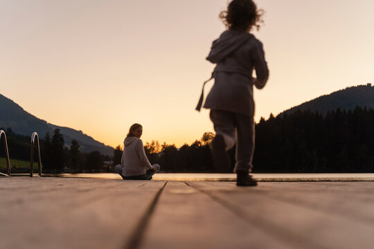 Little girl running toward mother sitting at edge of lakeshore jetty at dusk