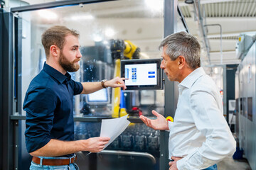 Two men discussing in a production hall with industrial machinery and a tablet