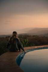 Tourist touching water in infinity pool enjoying sunset over valley in tanzania, africa, during...