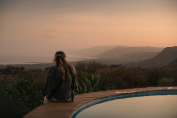 Tourist contemplating sunset over lake manyara from a lodge with swimming pool during a safari trip...