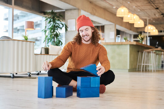 Mid adult man playing with toy block while sitting on floor in living room at home