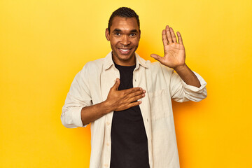 African American man with shirt, yellow studio, taking an oath, putting hand on chest.