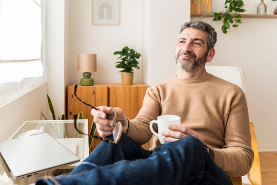 Man sitting indoors with a cup, looking relaxed and contemplative - Powered by Adobe