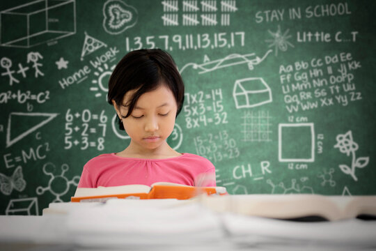 Asian schoolgirl reading a book in classroom