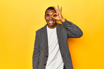 African American man in casual blazer, yellow studio, excited keeping ok gesture on eye.