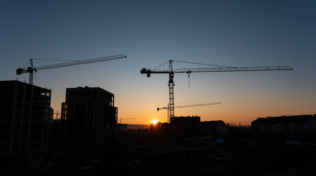Construction cranes at sunset over a city skyline creating a tranquil yet industrious atmosphere