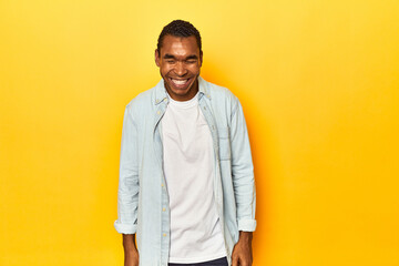 Fototapeta premium African American man in blue shirt, yellow studio, laughs and closes eyes, feels relaxed and happy.