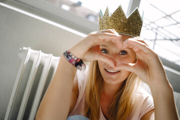 Portrait of blond young woman wearing a crown shaping a heart with her hands