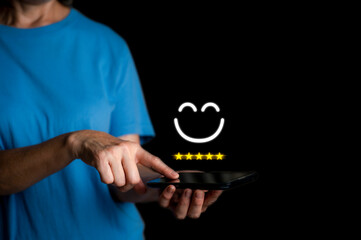Close up woman hand holding smart phone and show the smile face emoticon on the virtual touch screen ,give five star symbol, Customer service and business satisfaction survey.