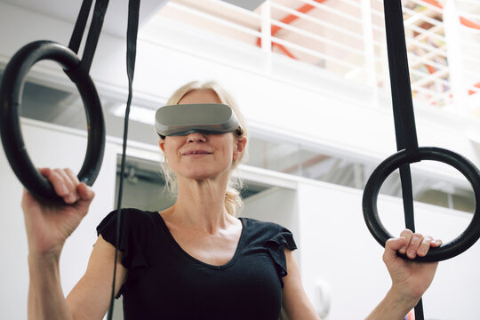 Woman using virtual reality headset while exercising with gym rings indoors