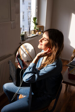 Woman enjoying sunlight indoors while using a smartphone