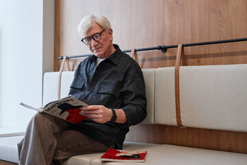 Stylish man reading magazines on a sofa in a minimalist interior