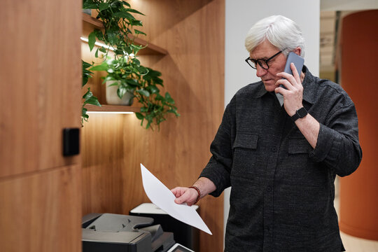 Busy man talking on mobile phone while checking papers in office