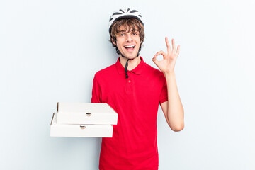 Young delivery caucasian man holding pizzas isolated on blue background cheerful and confident...