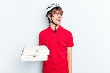 Young delivery caucasian man holding pizzas isolated on blue background looks aside smiling,...