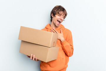 Young man making a move while picking up a box full of things isolated on blue background laughs...