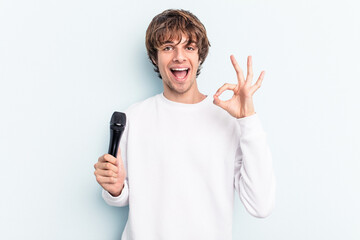 Young caucasian singer man isolated on blue background cheerful and confident showing ok gesture.
