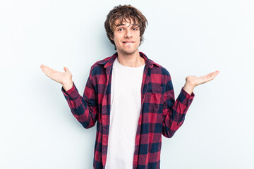 Young caucasian man isolated on blue background confused and doubtful shrugging shoulders to hold a...