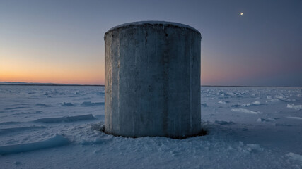 Naklejka premium Concrete cylinder rising from frozen arctic landscape at sunset with moon in the sky